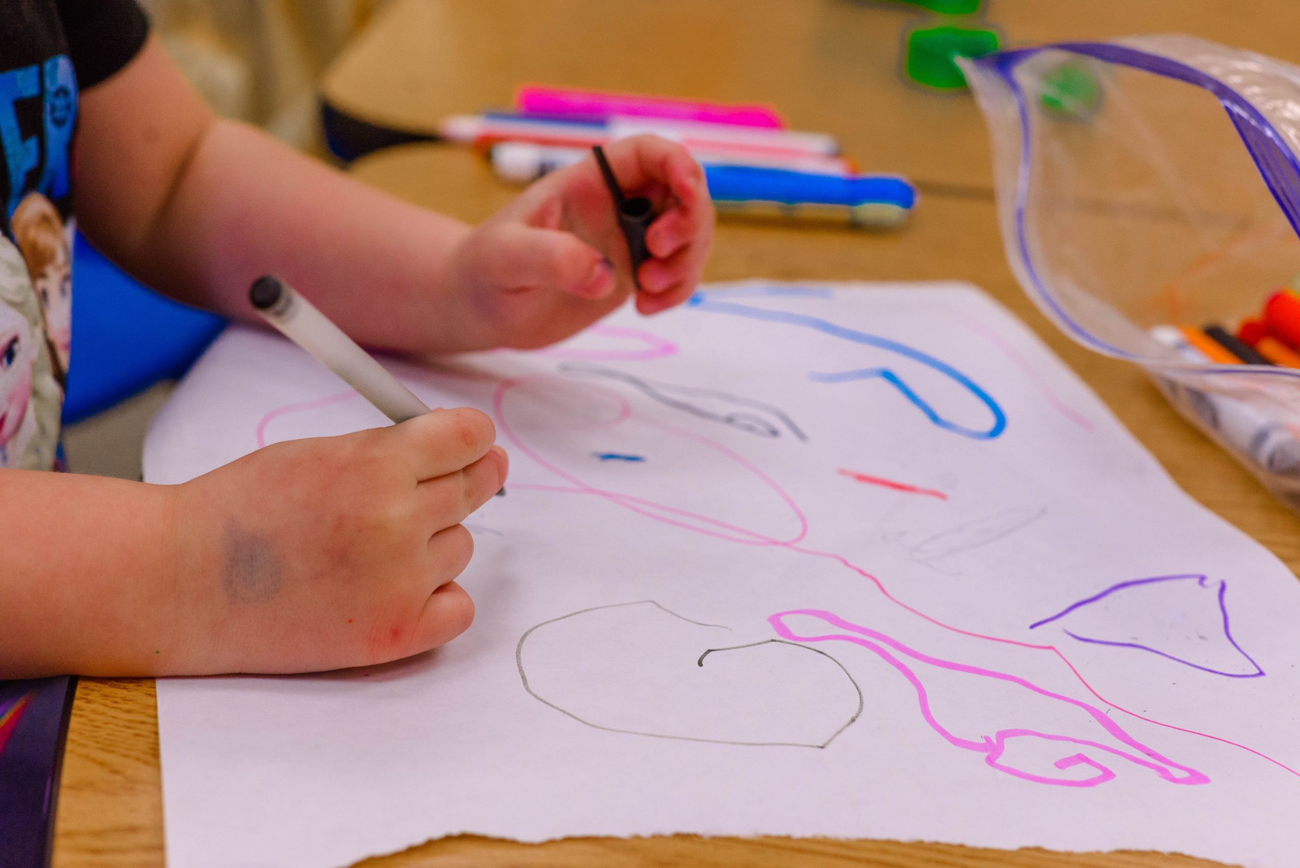 close up photo of a child's hands drawing colored shapes on a large scrap of paper