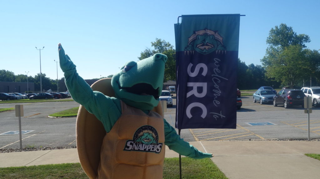Sheldon (SRC mascot) standing near Welcome to SRC flag