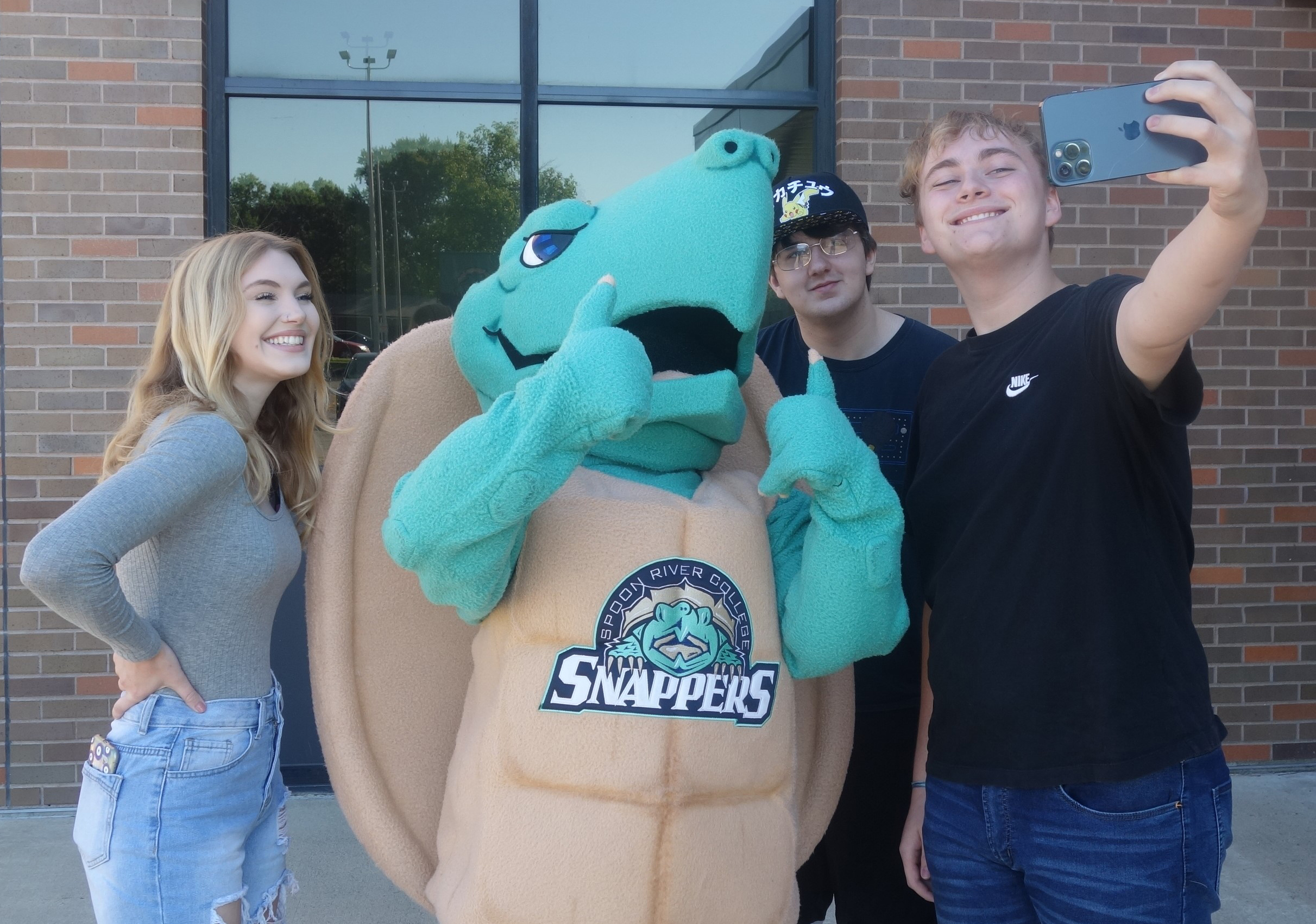 three students taking selfie with SRC mascot, Sheldon