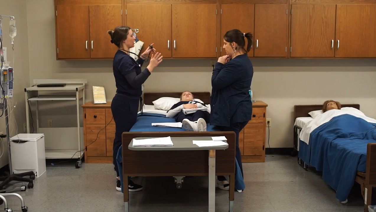 Nursing faculty and students working together in patient lab