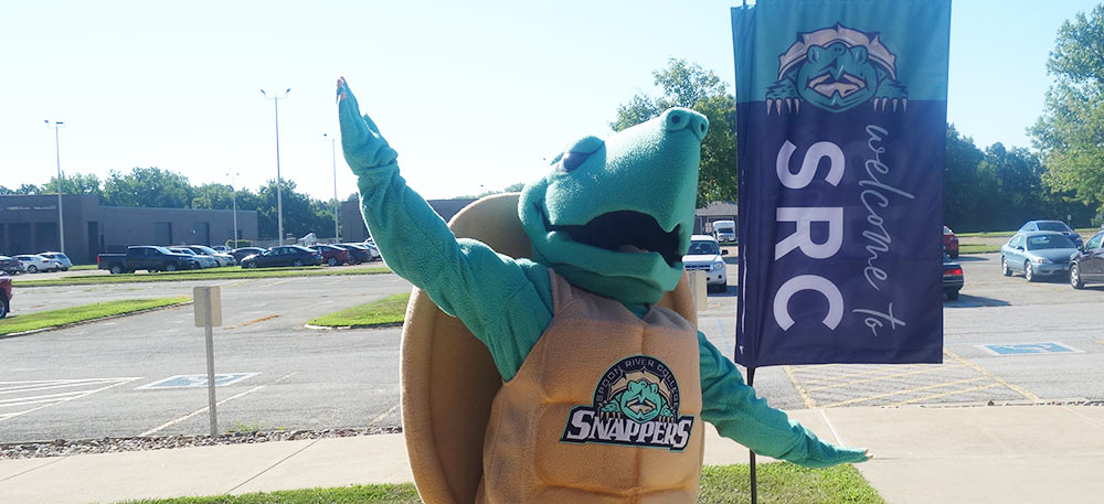 SRC's mascot Sheldon standing in front of a Welcome to SRC flag