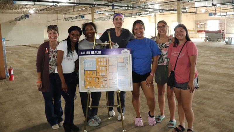 Group of students, faculty and staff in the area where the Allied Health wing will be, with a floor plan of the planned layout.