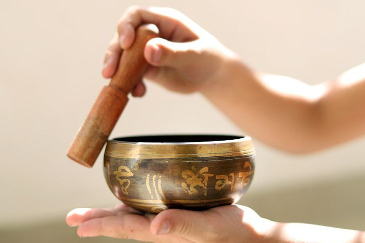 Tibetan singing bowl resting on the palm of a hand with the other hand holding the stick against the edge of the bowl