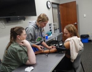 Student taking a blood pressure reading on another student while an instructor watches