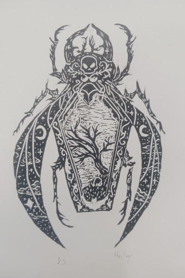 Printmaking: Beetle by Hailey Ford. A detailed black-and-white linocut or woodblock print of a stylized beetle. The beetle's body is rendered as an elaborate decorative composition: a coffin shape on the thorax contains a bare tree and a skull, flanked by crescent moons and stars. The large curved forelegs and mandibles are adorned with intricate scrollwork. The overall effect is ornate and gothic.