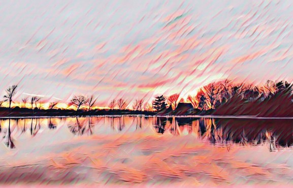 Photograph (digitally stylized): Winter by Carl Moreland. A wide landscape image of a lake at sunset or sunrise in winter. Bare trees and a farmhouse are silhouetted on the far bank. The sky is filled with dramatic, sweeping streaks of pink, coral, and pale gold — rendered in a painterly, textured style that makes the clouds appear like bold brushstrokes. The scene is perfectly mirrored in the still water below.